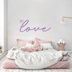 a bed with pink sheets and pillows in front of a wall that says love