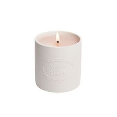 a small white candle holder with a single lit candle in the center and an oval label on it