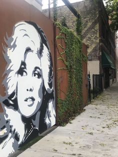 a wall with a painting of a woman on it next to a sidewalk in front of a building