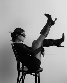 a woman sitting on top of a chair with her legs up and wearing high heeled boots