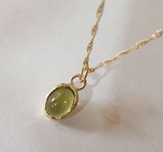 This minimalist Green peridot, solid gold necklace was designed with a bottle green see through pendant, to beautifully accompany you through your busy days. The classic simple design is always pretty for day and evening, work or fun. The gold Tourmaline necklace is handmade and delicate and available both with a 9kt or a 14 karat pendant. The solid gold chain is made of 14k and available in a couple of lengths. The clear Green Peridot necklace is a perfect chic and elegant gift. The pendant can be ordered without the necklace too. It can also be ordered in other gems. The model is wearing the same necklace set with a beautiful aquamarine. Dimensions: Oval pendant length is 1 cm (0.4 inch) and 8mm (0.3 inch) wide. The peridot is 6x8mm in either cabochon or facet cut. Please note that the s Emerald Gold Necklace, Acubi Style, Green Stone Pendant, Peridot Pendant, Peridot Necklace, Solid Gold Necklace, Solid Gold Chains, August Birthstone, Tourmaline Necklace