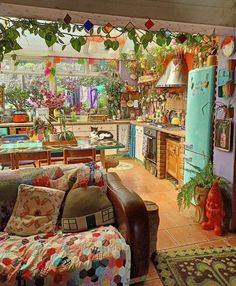 a living room filled with furniture and lots of plants hanging from the ceiling next to a kitchen