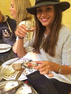 a woman sitting at a table holding a wine glass and oyster in front of her