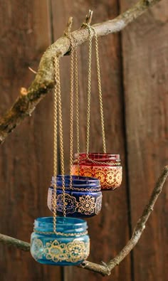 four jars hanging from a tree branch with chains attached to the top one is blue, red and yellow