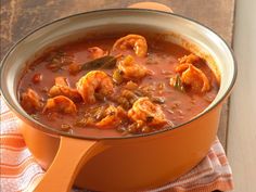 a bowl of soup with shrimp in it on a towel next to an orange pot