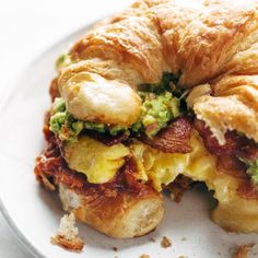 a croissant sandwich with bacon, eggs and avocado on it sitting on a plate