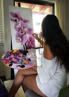 a woman sitting in front of a painting on a easel with flowers painted on it