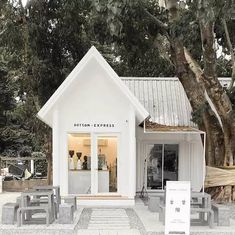 a small white building sitting next to a forest filled with lots of trees and benches