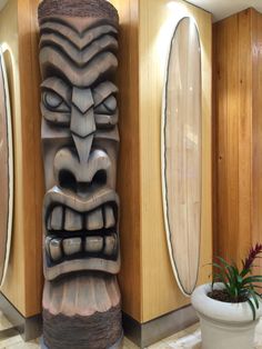 a tiki statue next to two planters in a room with wood paneled walls