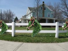 three wreaths are hanging on the white picket fence in front of a blue house