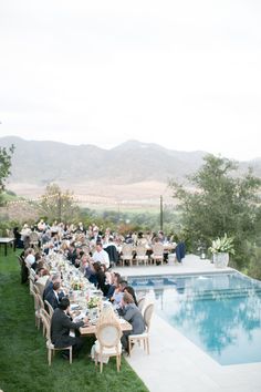 a group of people sitting around a table near a swimming pool with mountains in the background