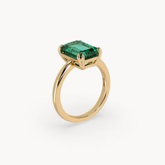 a gold ring with an emerald colored stone in the center, on a white background