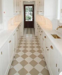 a long kitchen with white cabinets and checkered flooring on the walls, along with an open door leading to another room