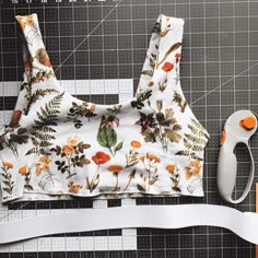 a pair of scissors next to a floral print crop top with white ribbon on it