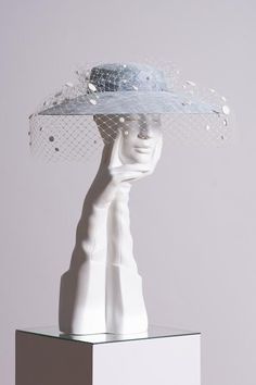 a white sculpture with a blue hat on it's head and veil over its face