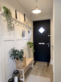 a black door is next to a white wall and some plants are on the shelf