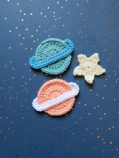 three crocheted space objects sitting on top of a blue surface with gold stars