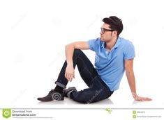 a man sitting on the ground with his legs crossed, wearing glasses and a blue shirt