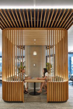 two people sitting at a table in an office with wooden slats on the walls