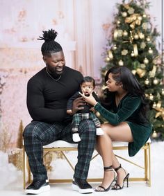 a man and woman sitting on a bench with a baby in front of a christmas tree