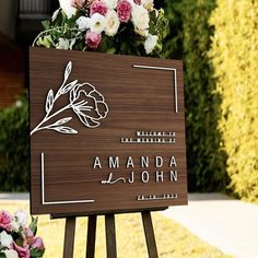 a wooden sign with flowers on it sitting in front of a bush and building that says amandaa john