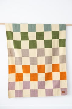 an orange, green and white checkered blanket hanging on a clothes line against a white wall