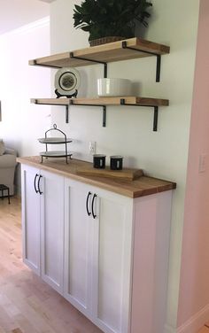 a kitchen with white cabinets and wooden shelves on the wall next to a potted plant