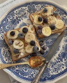 two pieces of bread with bananas and blueberries on it, sitting on a plate next to a spoon