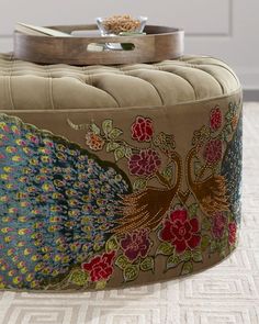 a round ottoman with a peacock design on the front and back cover, sitting on top of a carpeted floor