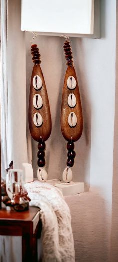 two wooden earrings hanging on the wall next to a table with a white curtain and window behind them