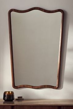 a wooden table with a mirror on top of it next to a vase and candle