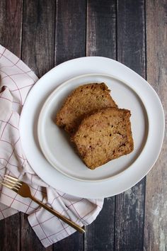 two pieces of bread on a white plate next to a fork and napkin with a wooden background