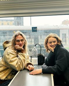 two women sitting at a table in front of a window