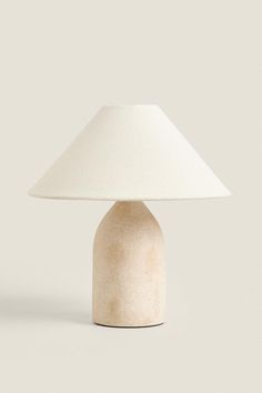 a table lamp with a white shade on the top and bottom, sitting against a gray background