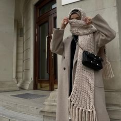 a woman is standing on the steps wearing a scarf and coat with a handbag