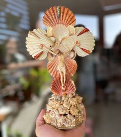 a hand holding a small statue of a woman with seashells on her head