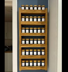 a wooden shelf filled with lots of jars on top of a blue wall next to a white door