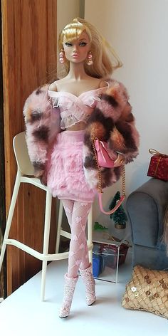 a barbie doll dressed in pink and brown furs holding a handbag while standing next to a chair