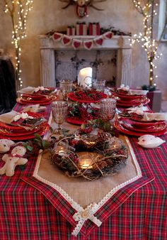 the table is set for christmas dinner with red and white plates, silverware, and candles