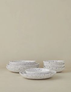 five white bowls with speckles are stacked on top of each other in front of a beige wall