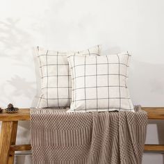 two pillows sitting on top of a wooden bench next to a blanket and pine cones