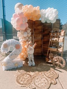 two people standing next to a large number 2 balloon arch in front of a fence