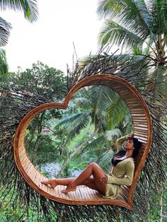 a woman laying in a heart shaped hammock surrounded by palm trees and greenery