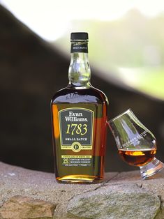 a bottle of whisky sitting next to a glass on a stone wall with grass in the background