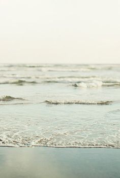 a woman standing on the beach holding a surfboard in her hand and looking out at the ocean