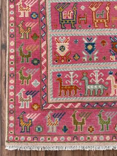 a pink rug with animals on it and fringes hanging from the floor in front of a wooden wall