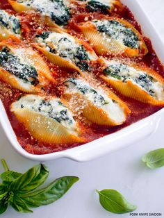 a white casserole dish filled with ravioli and spinach covered in parmesan cheese