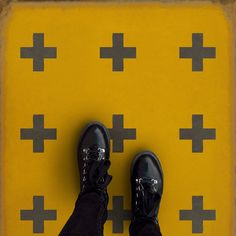 a pair of black shoes standing on top of a yellow and gray floor with crosses