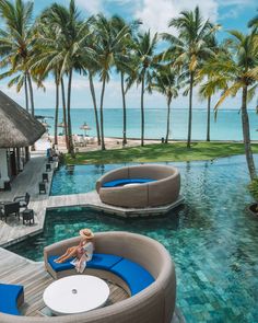 a woman sitting on the edge of a pool next to some lounge chairs and palm trees