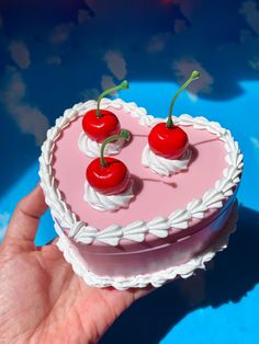 a heart shaped cake with cherries on top is being held by someone's hand